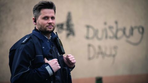 Polizeihauptkommissar Lukas Serafin steht vor Hauswand mit Graffiti in Duisburg.